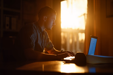 A student engrossed in a laptop, bathed in warm light, symbolizing focused learning in affiliate marketing.
